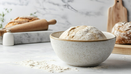 Fototapeta premium Bowl of fresh yeast dough with flour, rolling pin and fresh sourdough bread on white stone background. Baking, pastry concept
