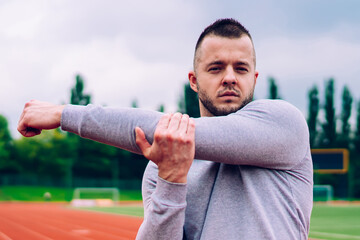 Confident young sportsman stretching bicep on track