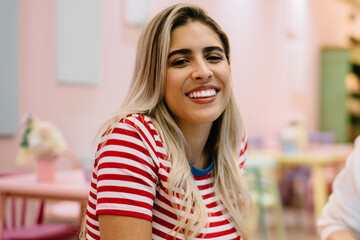 Portrait of cheerful Hispanic hipster girl laughing at camera during collaborative meeting with blurred freelance colleague, happy female students 20 years old enjoying e learning togetherness