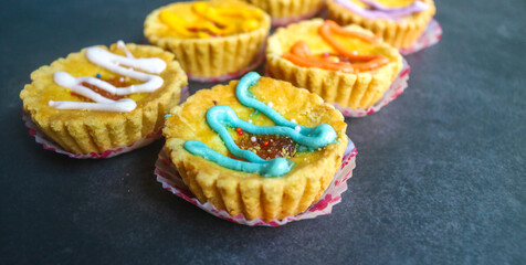 Set of variety mini pies with colorful toppings on a white plate. small tart cakes and pies on gray background with orange napkin, top view