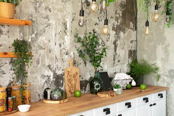 Interior scandi open cuisine. Wooden shelves with various cookware, plants in pots and decoration in the kitchen. Loft pendant Edison light bulbs lamps on background of rough cement plaster on wall.	
