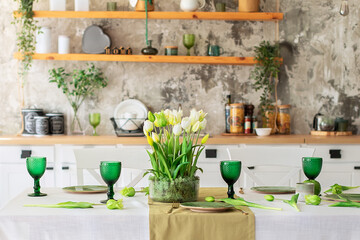Table festive setting with tulips flowers and stabilization moss in glass vase. Wedding table decoration. Beautiful served table with runner on table, wineglass and plates in living room	
