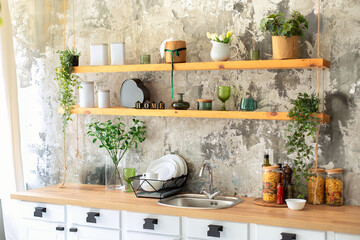 Stylish scandi white cuisine interior decor. Ceramic plates, green plants in pots, dishes and cozy decor on wooden shelves. Kitchen wooden shelves with various cookware. Open shelves in the kitchen.	
