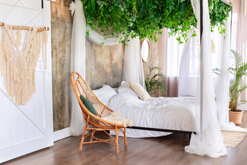 Interior boho design bedroom with garland flowers and plants. Cozy light bedroom in Scandinavian style bedroom, canopy bed and wicker rattan armchair. Bed decorated flowing white curtains canopies.   © stock_studio