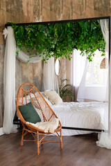 Interior boho design bedroom with garland flowers and plants. Cozy light bedroom in Scandinavian style bedroom, canopy bed and wicker rattan armchair. Bed decorated flowing white curtains canopies.   © stock_studio