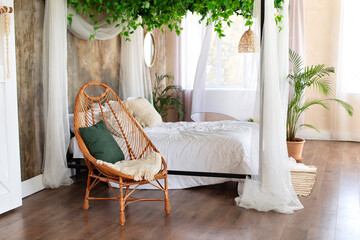 Interior boho design bedroom with garland flowers and plants. Cozy light bedroom in Scandinavian style bedroom, canopy bed and wicker rattan armchair. Bed decorated flowing white curtains canopies.   © stock_studio