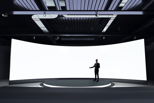Modern presentation stage with a businessman in front of a curved blank digital screen in a dark, contemporary exhibition space.