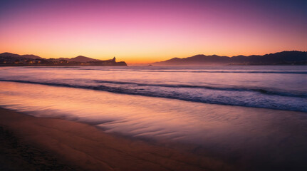 Fototapeta premium Beautiful sunset over the ocean with waves lapping on the sandy beach at dusk