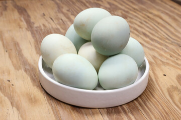 A Stack of Pale Green Chicken Eggs in a White Bowl on a Wooden Table