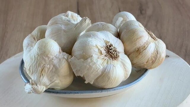Bowl of fresh organic garlic bulbs and cloves spinning on wooden cutting board. Close up. 