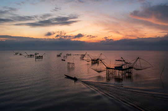 Silhouette of a boat sailing past traditional fishing nets and platforms on Pak Pra river at sunrise, Phatthalung, Thailand
