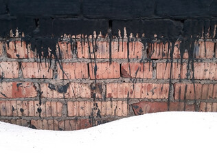 Old brick wall with streaks of waterproofing. Fragment of brick foundation in snow.