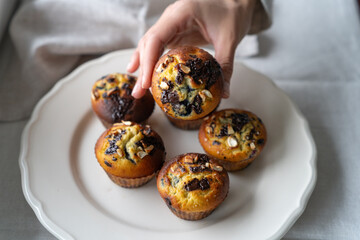 Close-up of a person reaching for a coconut flour muffins with assorted nuts and dark chocolate chips