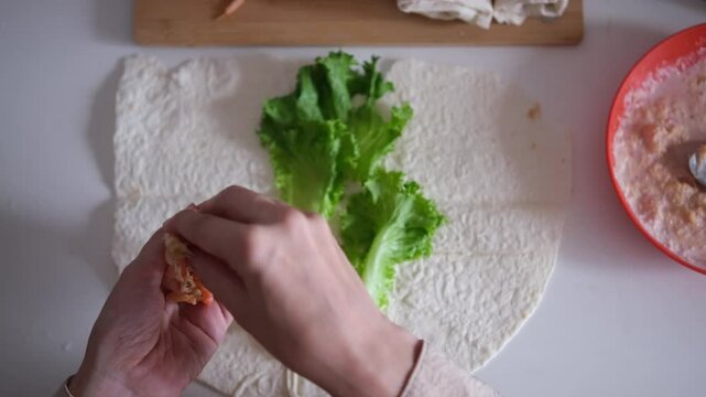 Female hands preparing a wrap with fresh lettuce, tomatoes, sauce and shrimp on a flat tortilla. Part of series