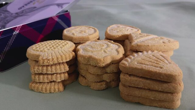 A closeup slow dolly shot of an assortment of crumbly Scottish shortbread biscuits, made with wheatflour and butter, next to the product tin container.