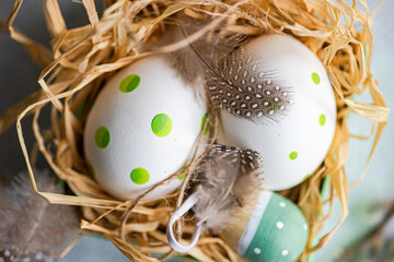 Close-up overhead view of a straw bird's nest with painted Easter eggs, pussy willow branches and quail feathers on a table