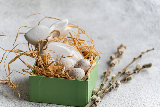 Close-up of a straw bird's nest with a ceramic Easter bunny, painted Easter eggs and pussy willow branches on a table
