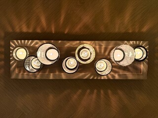 Overhead view of assorted glass candleholders with tealight candles casting shadows on a wooden table