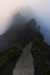 Bergspitze auf dem Pico do Arieiro auf Madeira, teils vom Nebel verdeckt, w&auml;hrend ein schmaler Weg sich durch die felsige Landschaft zieht und direkt auf den wolkenverhangenen Gipfel zuf&uuml;hrt