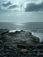 Beautiful sun shine on clouds and ocean on a summer day, in the foreground the beach with stones