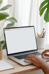 Fototapeta premium A person is typing on a laptop in front of a potted plant. The laptop screen is blank, and the person is using a pen and a pencil on a desk. Concept of productivity and focus