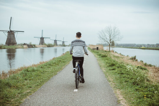Rear view of a Teenage boy cycling past a row of traditional windmills, Netherlands,