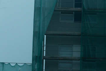 Building is under construction and features green protective netting draped across its facade for...