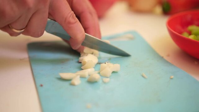 close up of unrecognizable male hands chopping garlic on board. Man's hands cutting garlic with a knife over cutting board. Making food at home, homemade