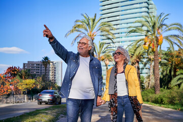 Carefree senior couple holding hands and walking in barcelona, enjoying a sunny day during vacation outdoors.
