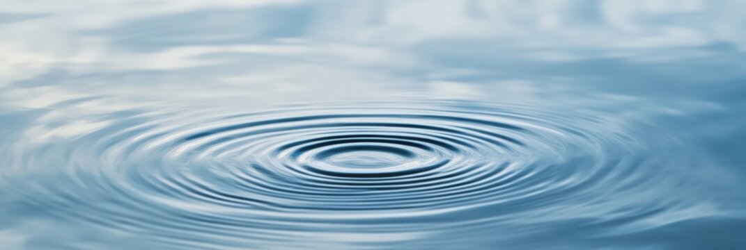 Gentle ripples expanding outwards on a calm water surface, creating concentric circles and reflecting the serene blue sky above, evoke a sense of tranquility and peace