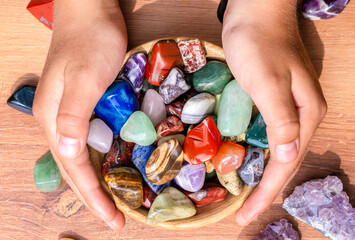 A cup with natural multi-colored minerals in the hands of a child and individual minerals on the...