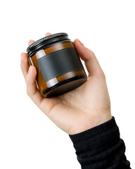 Aroma candle in brown glass jar with black lid in woman's hand. Isolate on white background. Copy space. Amber cylindrical candle design. Aromatherapy, kraft home decor, gift idea, relaxation.
