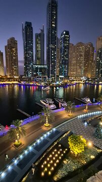 Panoramic view of Dubai Marina promenade at night. Night illumination with flashing lights, United Arab Emirates. Vertical video. High quality 4k footage