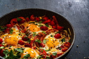 Shakshuka - fried eggs with vegetables in frying pan on black table