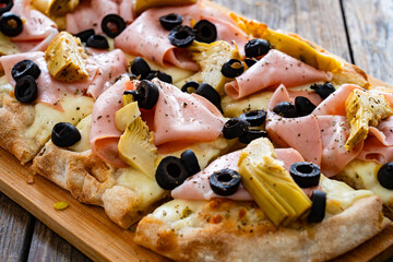 Roman Pizza with mozzarella cheese, boiled ham, black olives and artichokes on wooden table