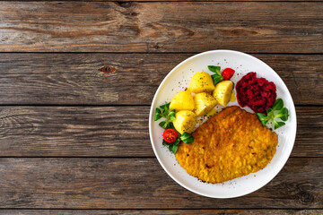 Breaded fried pork chop with boiled potatoes, fresh vegetables and beets on wooden table	