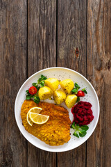 Breaded fried pork chop with boiled potatoes, fresh vegetables and beets on wooden table	