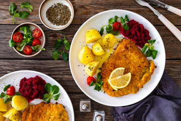 Breaded fried pork chop with boiled potatoes, fresh vegetables and beets on wooden table	
