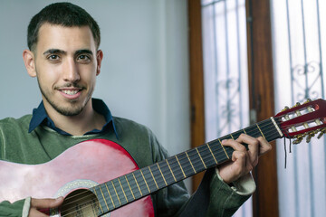 Obraz premium Young man playing red acoustic guitar, enjoying music at home