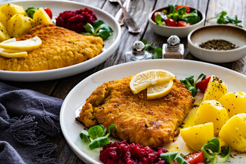 Breaded fried pork chop with boiled potatoes, fresh vegetables and beets on wooden table	