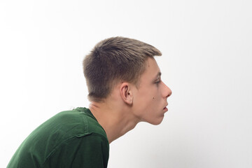 Obraz premium A close-up profile shot of a teenage boy. He has short, neatly styled brown hair and is wearing a simple dark green t-shirt. The background is plain white.
