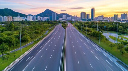 Obraz premium Asphalt highway with green mountains and a city skyline during sunset