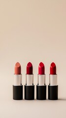Obraz premium Four elegant lipsticks in black and silver packaging arranged on a beige background, featuring a variety of shades from nude to deep red for beauty concepts