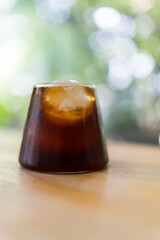 Close up of a black coffee with ice cubes in a clear glass on wood table