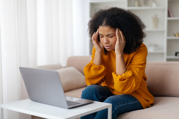 First symptoms of disease, migraine, overwork. Sad young african american female sits on sofa with...