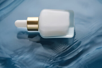 Bottle with white moisturizing serum in water on blue background.