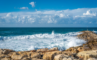 The surf crashes against the rocky shore and the vast sea stretches out under a beautiful sky dotted with clouds. The scene captures the beauty of nature where water meets land in perfect harmony.