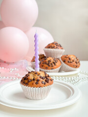 Chocolate chip muffin with pink balloon decorations and lit candle. Birthday concept