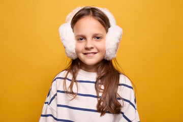 A young girl with brown hair smiles while wearing fluffy white earmuffs. The backdrop is a vibrant...