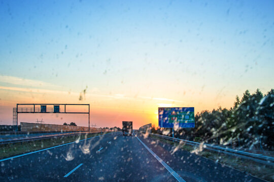 Blurry windshield sunset scene on a highway with cars and navigating signs, symbolizing road trips, navigation, and scenic journeys. Transportation, logistics, road traffic. Copy space
